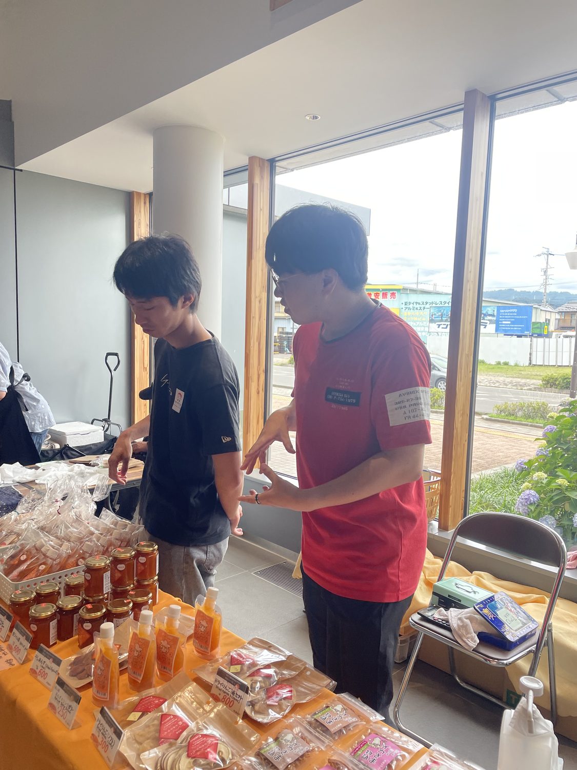売り場で来場者と会話する学生（手前にあんず加工品と値札）